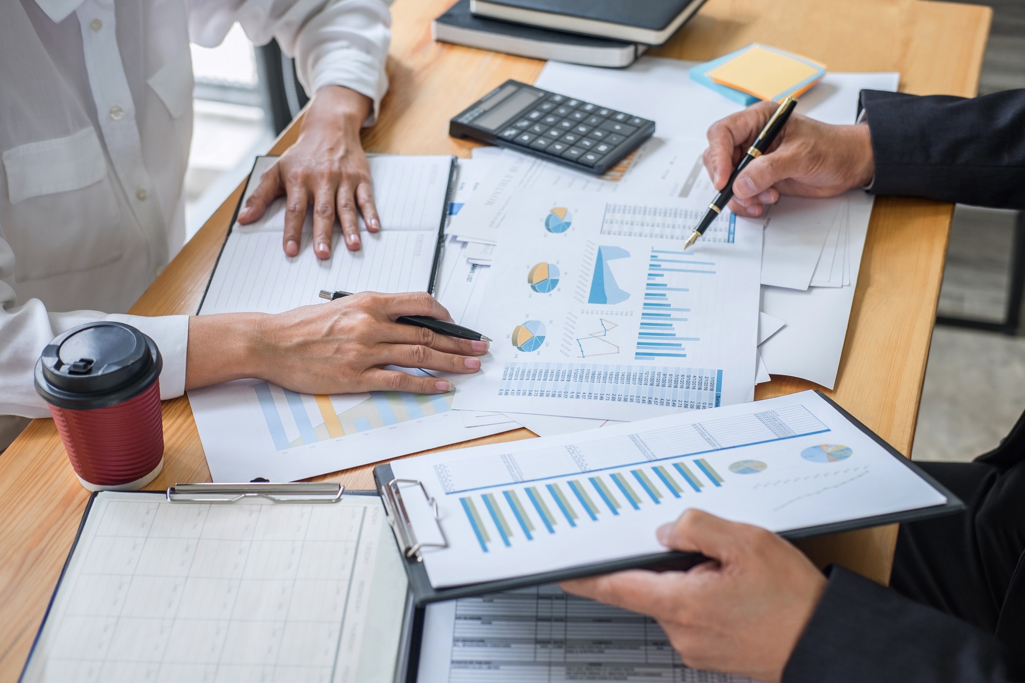 two people sitting Infront of a desk with both pointing at the graphs on the desk