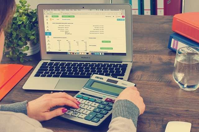 a person using a calculator Infront of a laptop on a desk